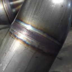 Szczegółowe zbliżenie spoiny na metalowej rurze wykonanej przez spawacza z Oławy, ukazujące charakterystyczne tęczowe zabarwienie i precyzyjne ułożenie ściegu.