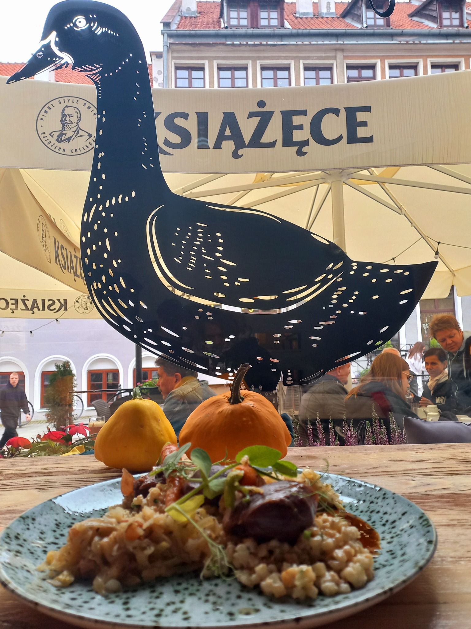 Danie na talerzu z dyniami w tle, widok przez okno kawiarni z dekoracją w kształcie czarnego ptaka.