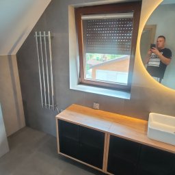 Marcin Jarosz - Nowoczesna łazienka na poddaszu z szarymi płytkami, grzejnikiem drabinkowym, szafką pod umywalkę z drewnianym blatem i okrągłym lustrem z podświetleniem LED, w którym odbija się osoba robiąca zdjęcie.