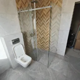 Nowoczesna łazienka po remoncie: kabina prysznicowa ze szklanymi drzwiami przesuwnymi, toaleta podwieszana i płytki imitujące marmur na podłodze i ścianach.