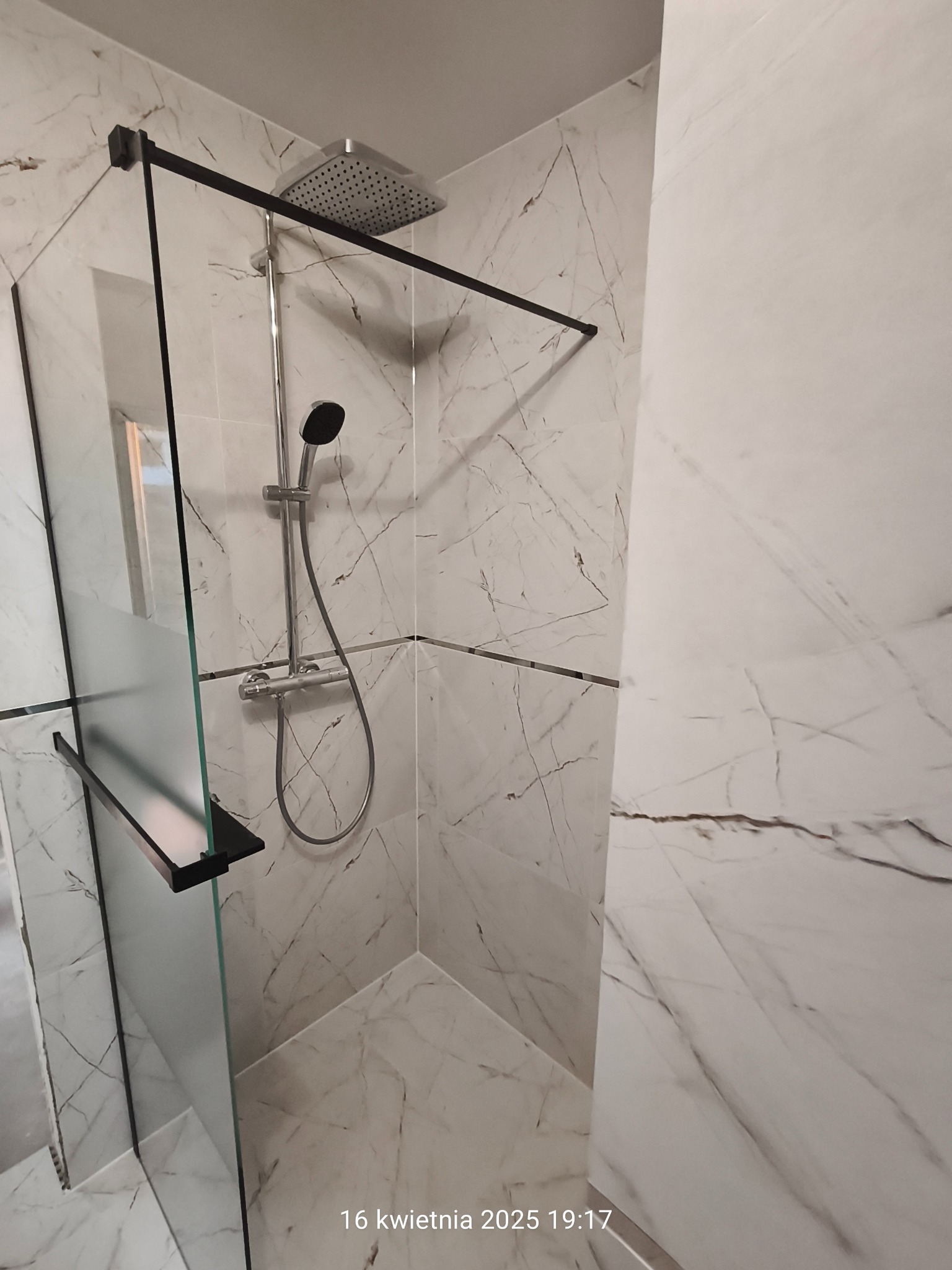 Kabina prysznicowa walk-in z czarnymi profilami i deszczownicą, wykończona płytkami imitującymi marmur. Nowoczesny design łazienki z minimalistycznym stylem.