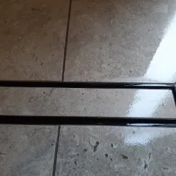 Beżowe płytki podłogowe z czarnym, liniowym odpływem prysznicowym, widoczne fugi.