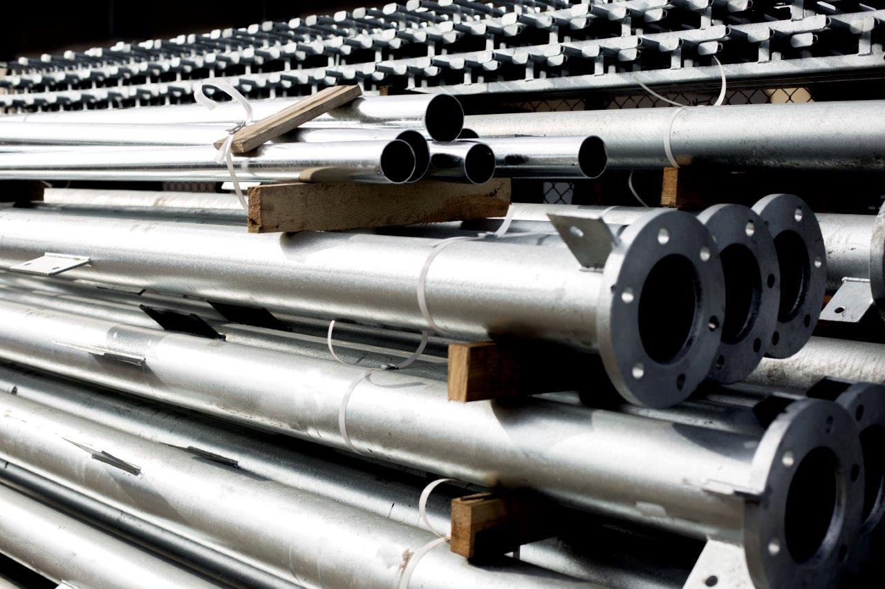 Stos ocynkowanych rur stalowych o różnych średnicach, z kołnierzami i uchwytami, oddzielonych drewnianymi przekładkami i spiętych taśmami.