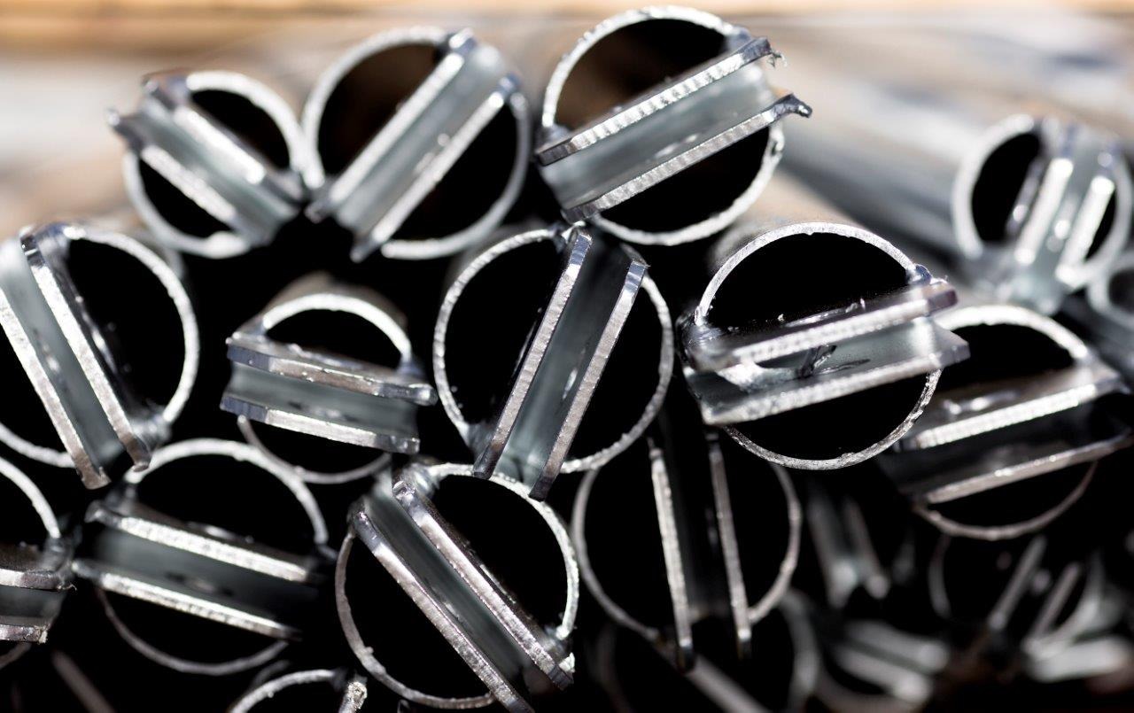 Stos rur stalowych z przyspawanymi uchwytami, widok z bliska na przekroje i elementy mocujące.