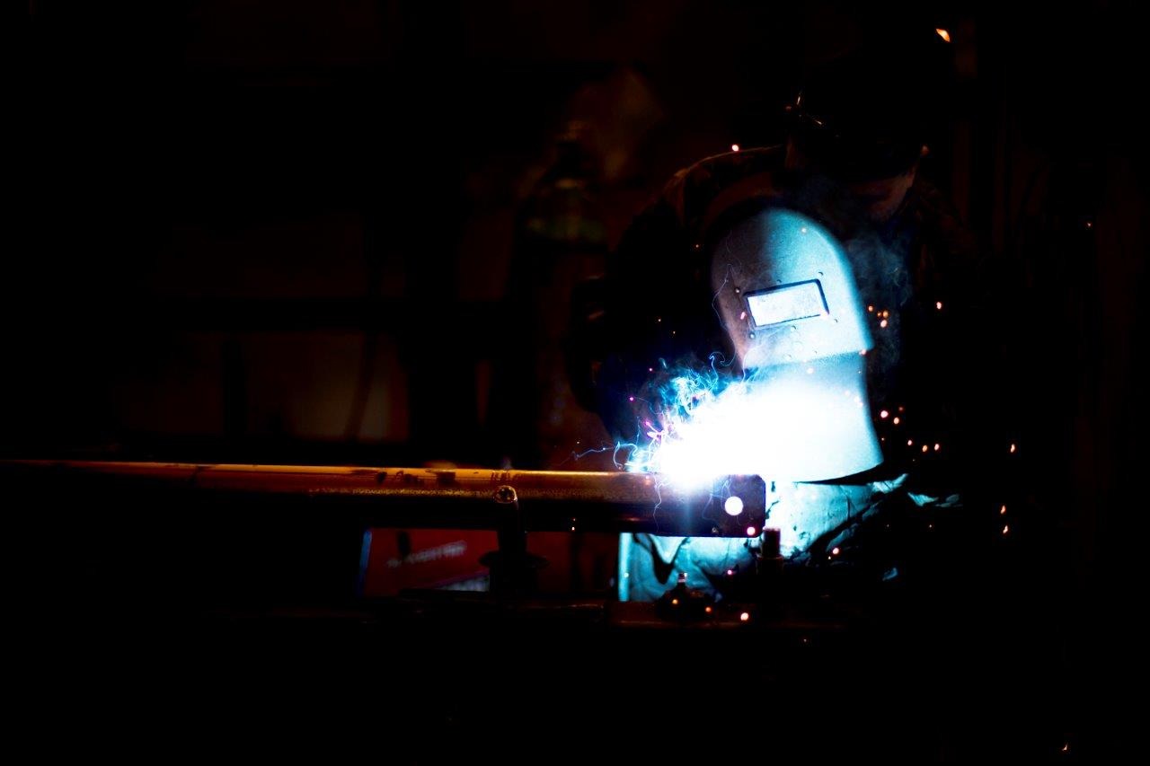 Spawanie rury w ciemnym otoczeniu, iskry i jasne światło łuku elektrycznego oświetlają maskę ochronną spawacza.