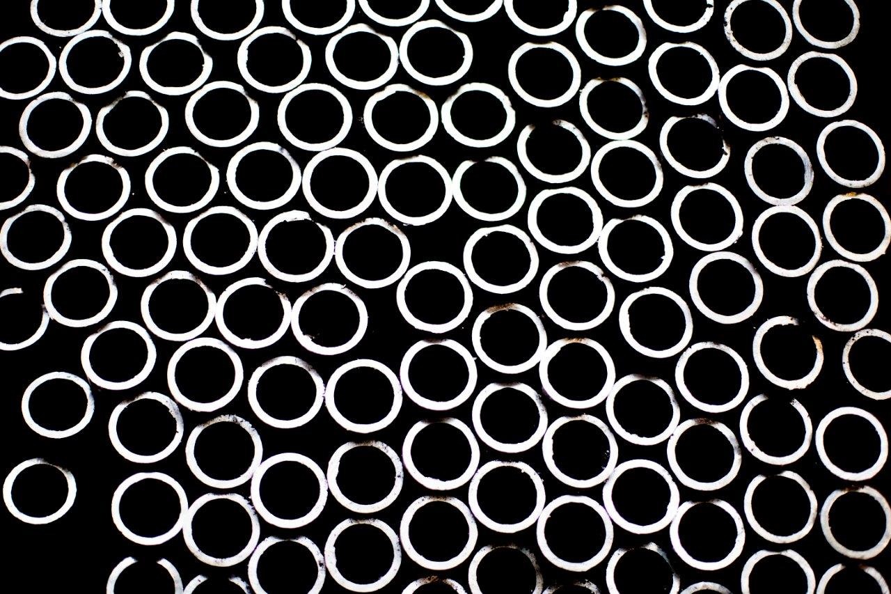 Stos białych, okrągłych rur stalowych na czarnym tle, widoczne ślady cięcia.