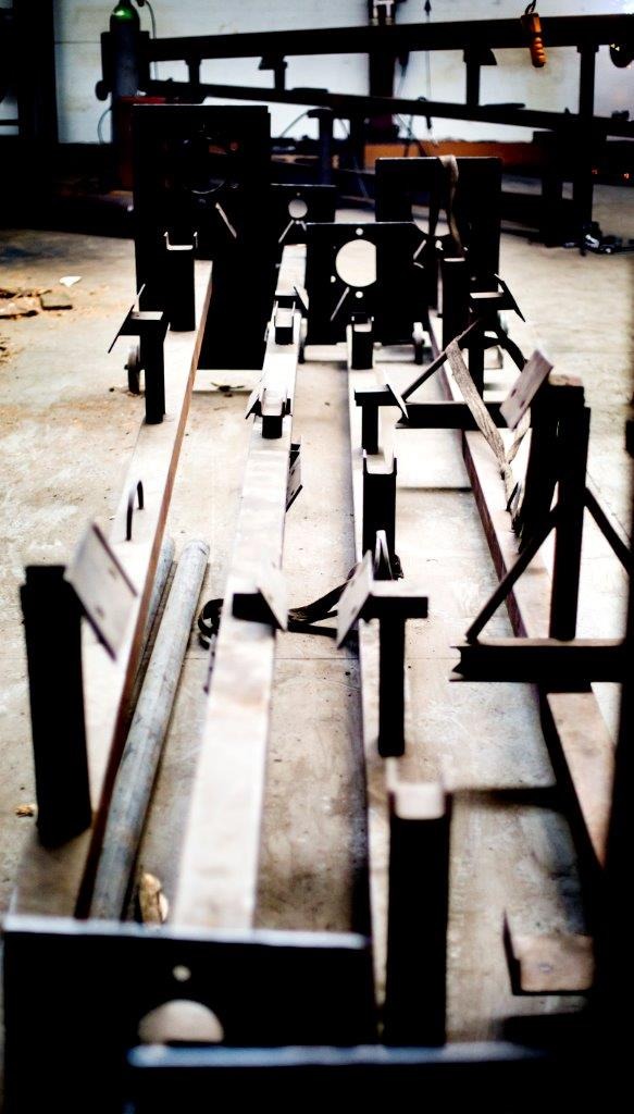 Elementy stalowe w warsztacie, przygotowane do spawania, widok w perspektywie z niskiego kąta, surowy beton na podłodze.