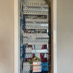 Otwarta skrzynka elektryczna z zainstalowanymi bezpiecznikami, przewodami i listwami zaciskowymi, widok od frontu.