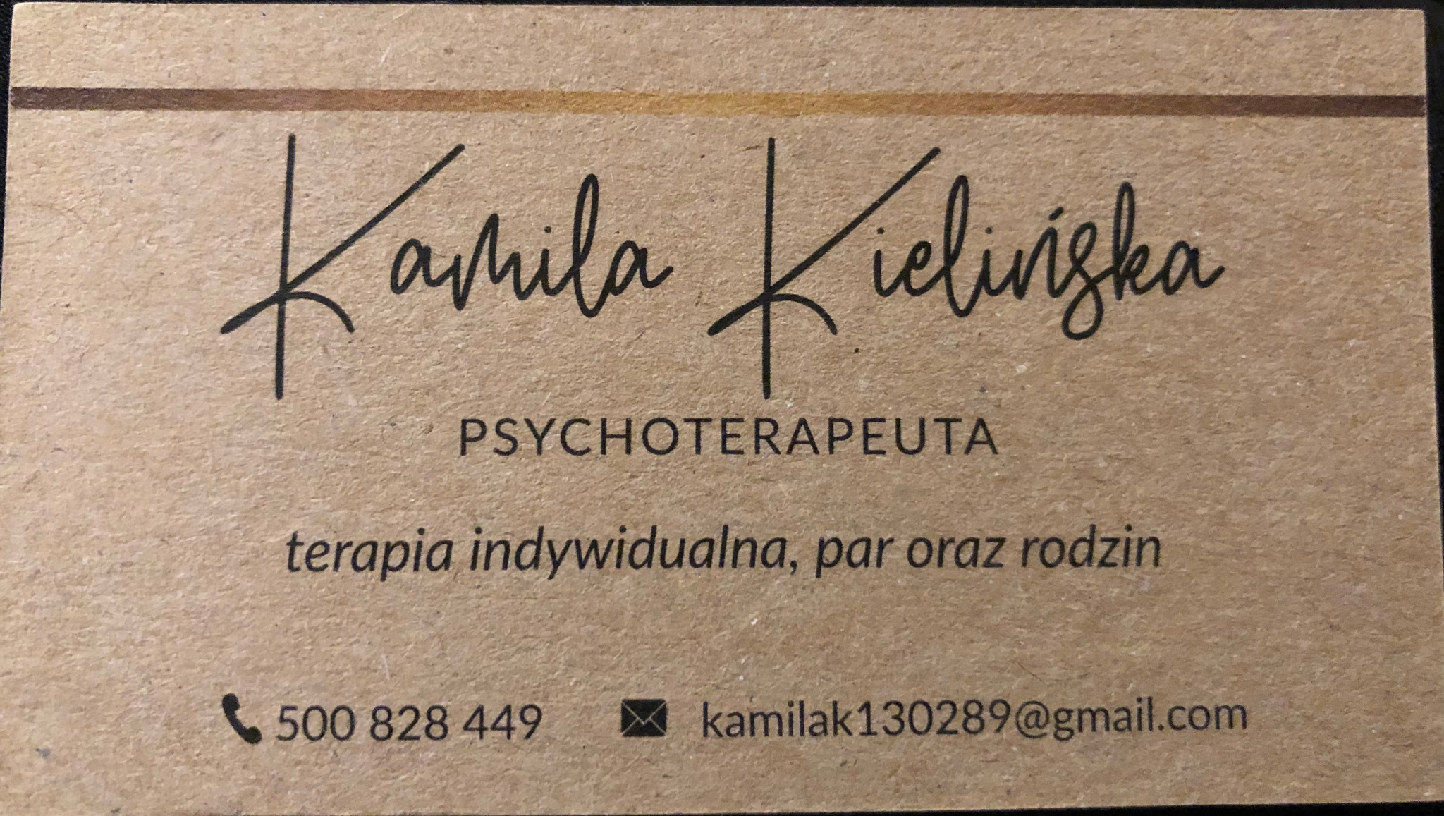 Wizytówka z imieniem i nazwiskiem Kamila Kielińska, tytułem PSYCHOTERAPEUTA oraz informacją o terapii indywidualnej, par i rodzin, numerem telefonu i adresem e-mail na tle papieru kraft.