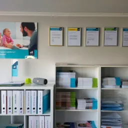 Biuro doradcy finansowego: regały z segregatorami oznaczonymi logo OVB, dyplomy w ramkach na ścianie, plakat z rodziną i hasłem 'Zapewnij sobie i swoim najbliższym bezpieczną przyszłość!'