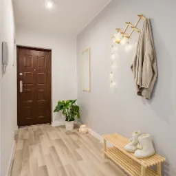 Jasny przedpokój z panelami podłogowymi imitującymi drewno, drewnianą szafką na buty i wieszakiem na ścianie, oświetlony girlandą z żarówek.