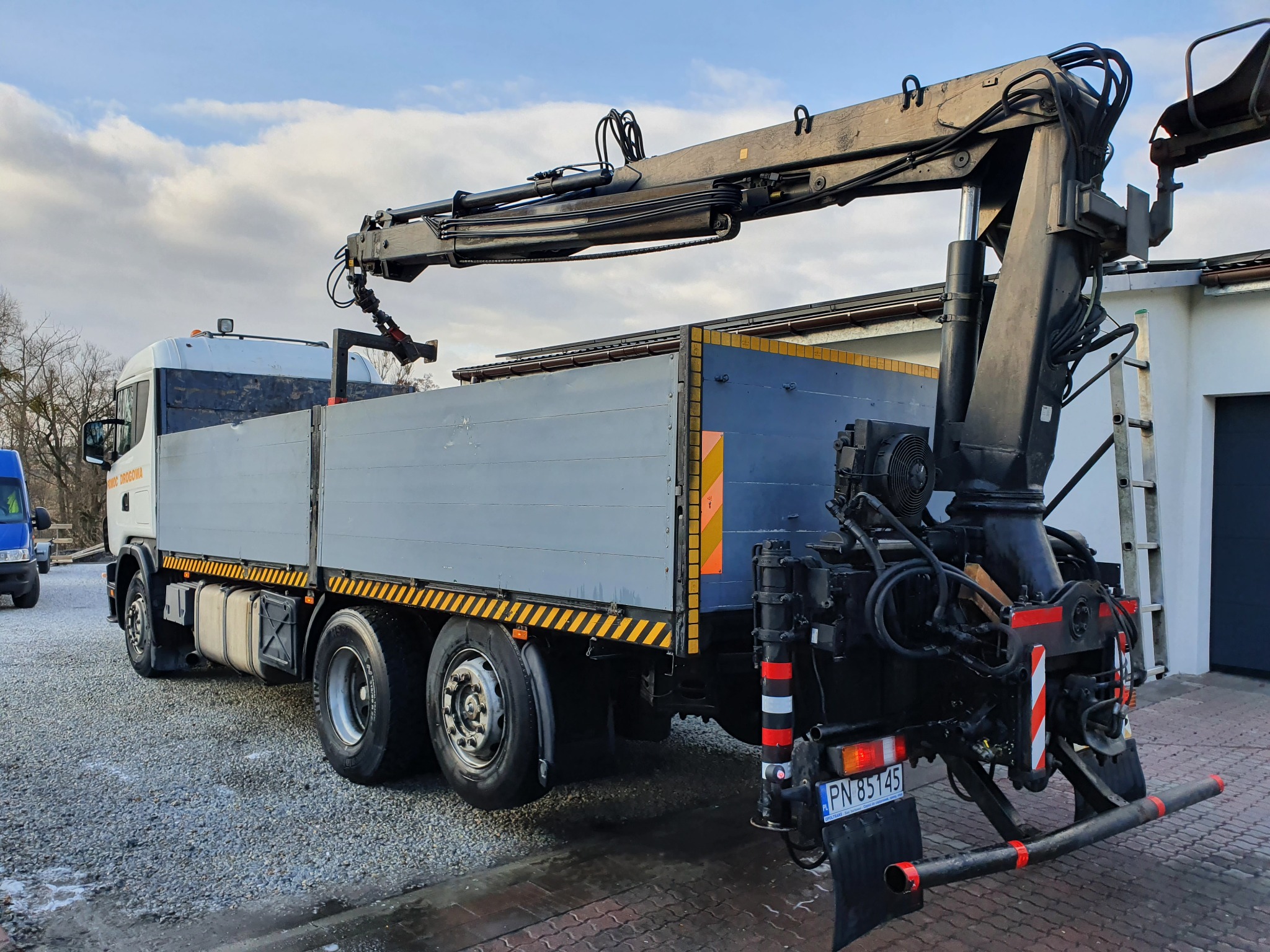 Laweta z wysięgnikiem hydraulicznym na podwoziu ciężarowym, widok z tyłu, zaparkowana na żwirowym podłożu, z widoczną tablicą rejestracyjną PN 85145.