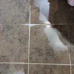 Czyszczenie fug na brązowych płytkach podłogowych, widoczna gąbka i ślady wilgoci.