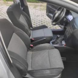 Wnętrze samochodu z widocznymi dwukolorowymi fotelami z tapicerką, widoczne ślady użytkowania na siedzeniach, otwarte drzwi kierowcy.