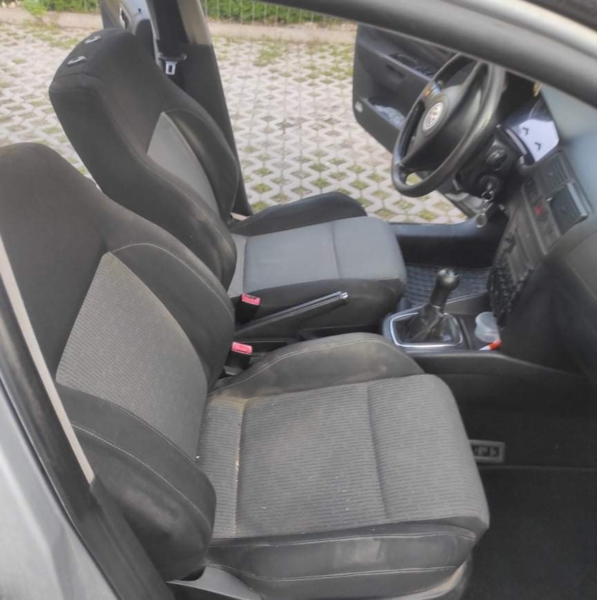 Wnętrze samochodu z widocznymi dwukolorowymi fotelami z tapicerką, widoczne ślady użytkowania na siedzeniach, otwarte drzwi kierowcy.