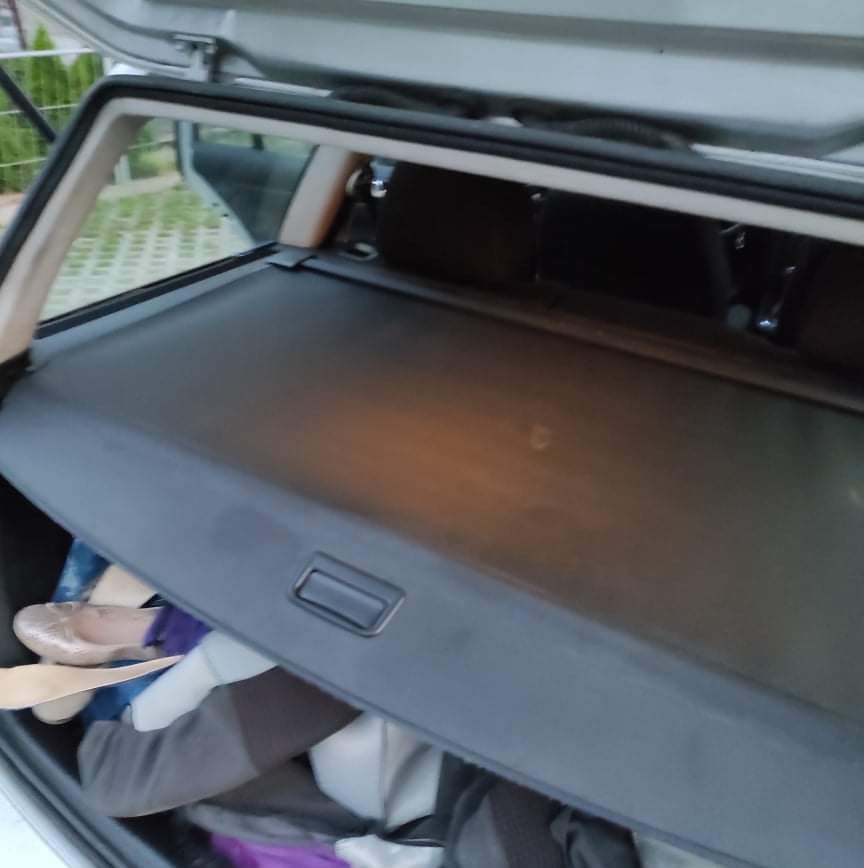 Widok z góry na bagażnik samochodu typu kombi z zasłoniętą roletą i częściowo widocznymi rzeczami pod spodem, w tym beżowe baleriny.