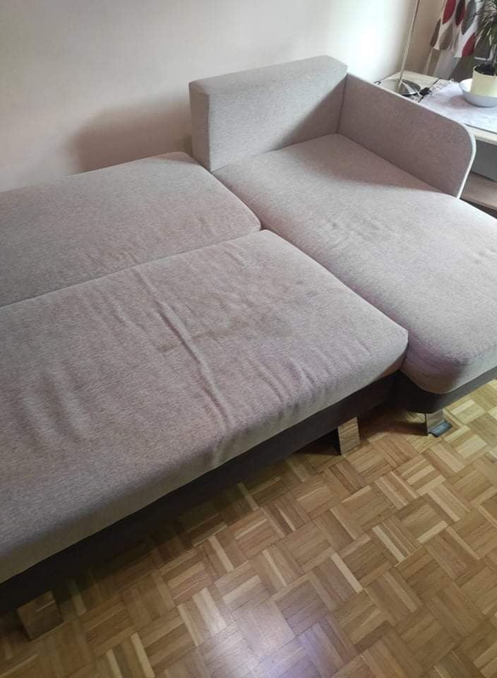 Jasnoszara, modułowa sofa z widocznymi plamami na siedzisku, stojąca na parkiecie ułożonym w jodełkę.