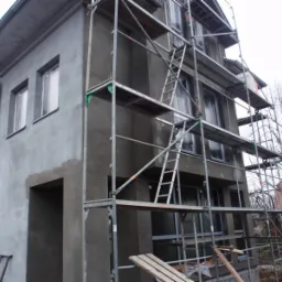 Dom w trakcie szpachlowania elewacji, widoczne rusztowania i świeżo nałożona szpachla na ścianach.