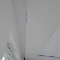 Białe, świeżo pomalowane wnętrze z widocznym oknem i fragmentem sufitu z lekkimi niedoskonałościami w wykończeniu, zabezpieczonym taśmą malarską.