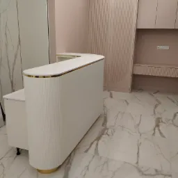 Biała lada z ryflowanym frontem i złotymi akcentami, dopasowana do zabudowy meblowej w pudrowym różu, na marmurowej podłodze.