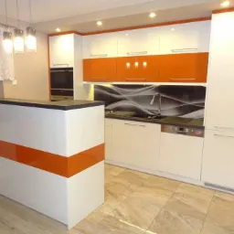 Nowoczesna kuchnia z białymi szafkami i pomarańczowymi akcentami, czarny blat, wyspa kuchenna z pomarańczowym pasem, wzorzysty panel nad blatem i podłoga z płytek imitujących drewno.