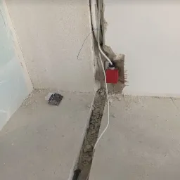 Bruzda w ścianie i podłodze w trakcie prac instalacyjnych, widoczne przewody elektryczne, puszka elektryczna i gruz.