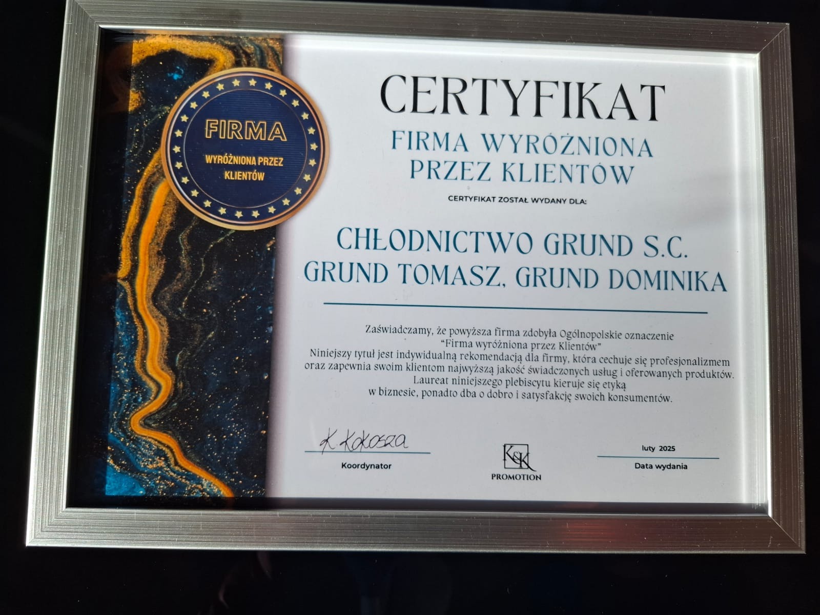 Oprawiony w srebrną ramkę certyfikat 'Firma Wyróżniona Przez Klientów' dla Chłodnictwo Grund S.C., z abstrakcyjnym, błękitno-złotym tłem po lewej stronie.