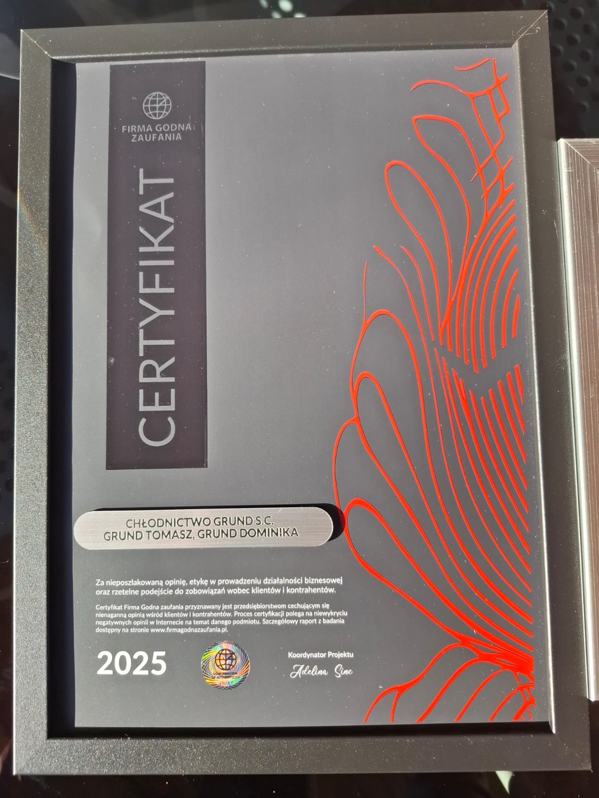 Oprawiony certyfikat 'Firma Godna Zaufania' dla firmy Chłodnictwo Grund S.C., z datą ważności do 2025 roku, z czerwonym abstrakcyjnym wzorem po prawej stronie.