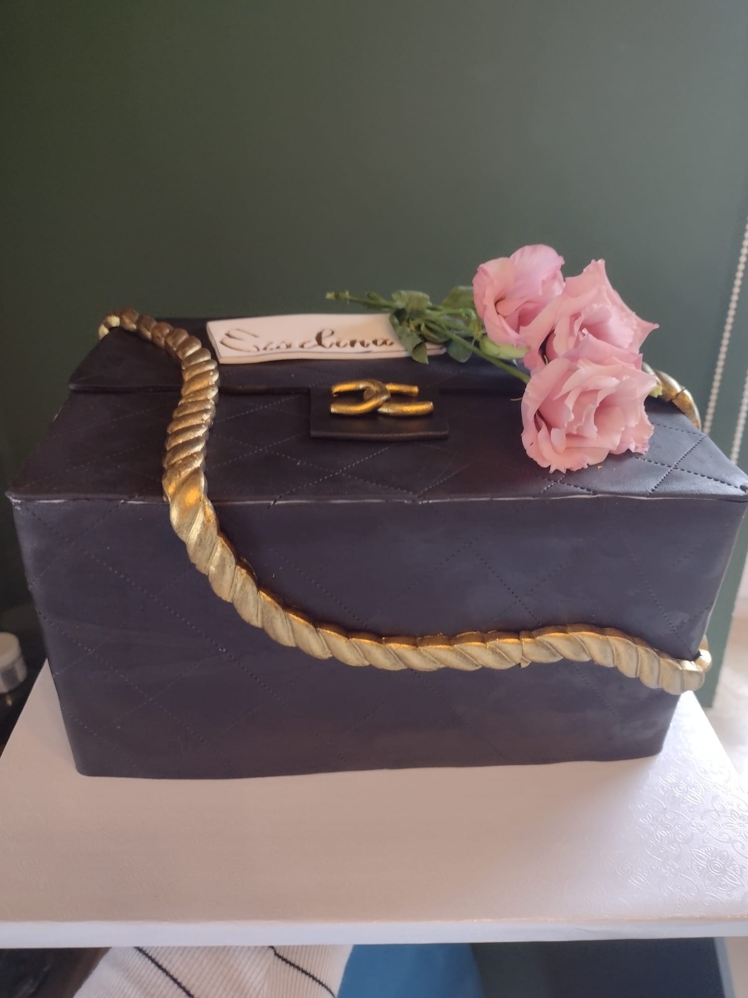 Tort w kształcie torebki damskiej, czarny z pikowaniem, złotym łańcuchem i różowymi kwiatami.