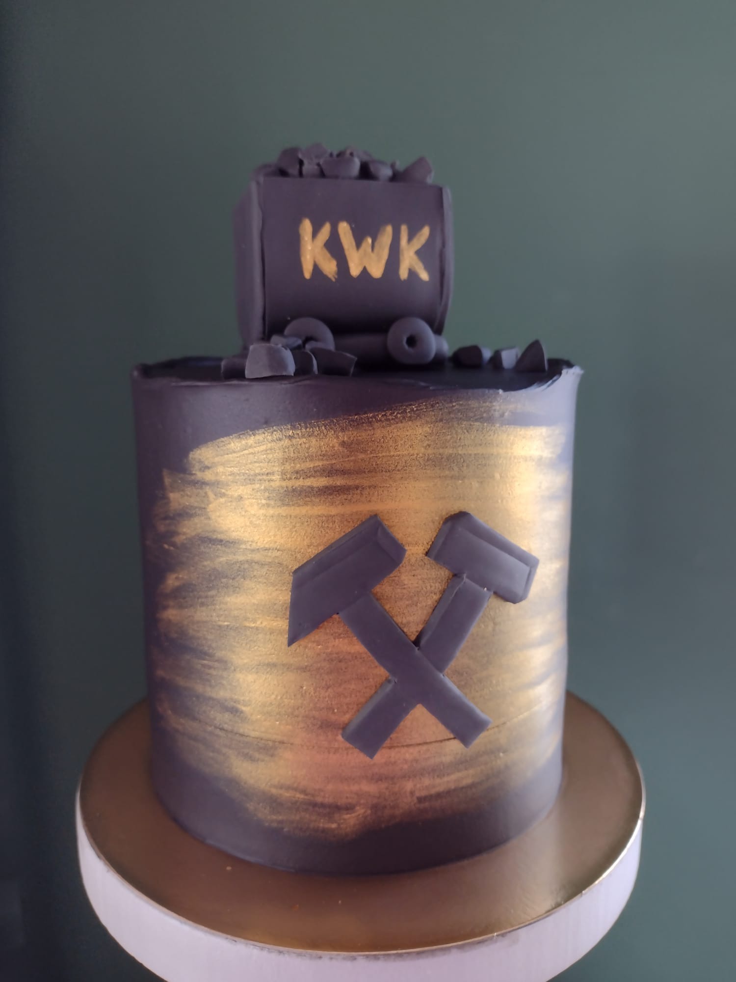 Tort w ciemnych barwach z motywem górniczym: wagonik węgla z napisem KWK i skrzyżowane młotki, dekorowany złotymi pociągnięciami pędzla.