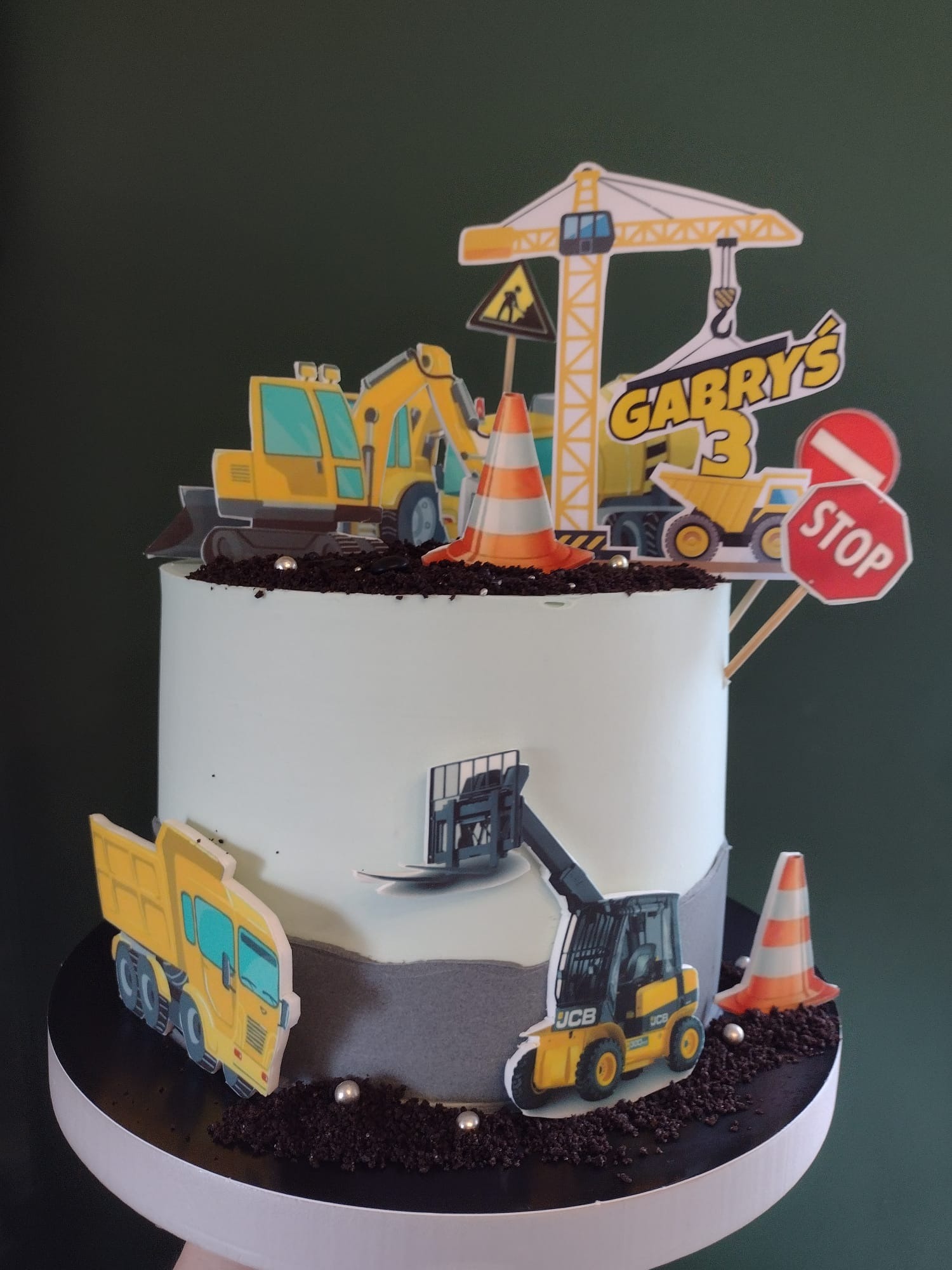 Tort urodzinowy z motywem budowy: dekoracje z papieru przedstawiają maszyny budowlane, znak stop i imię 'Gabryś' z cyfrą 3.