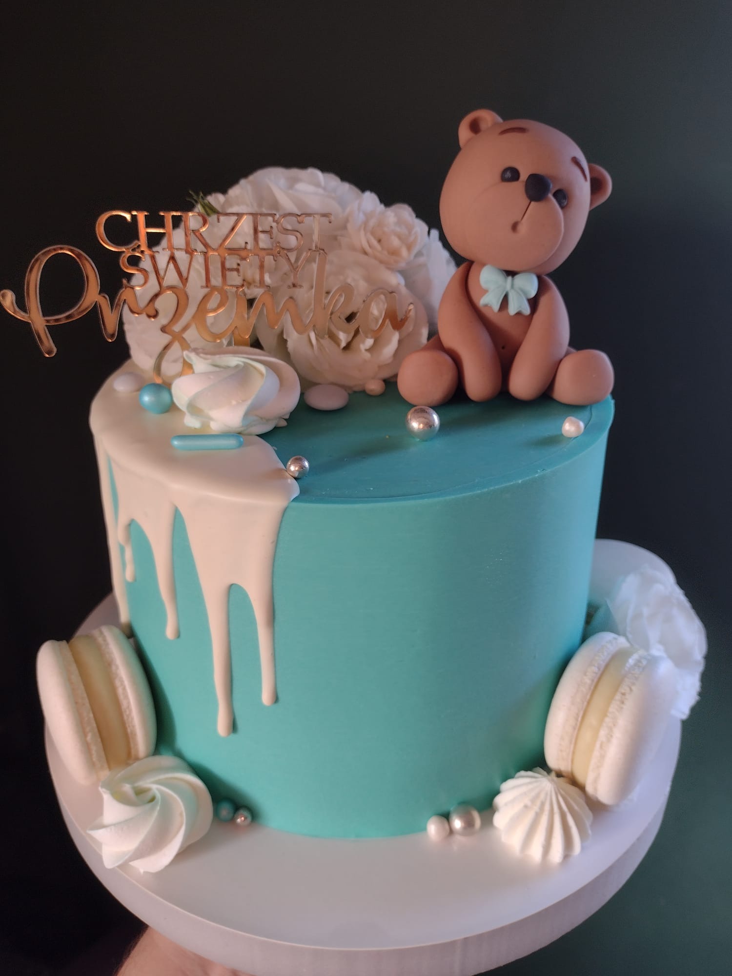 Tort na Chrzest Święty z turkusowym kremem, białymi makaronikami, bezami, topperem z napisem i misiem z lukru.