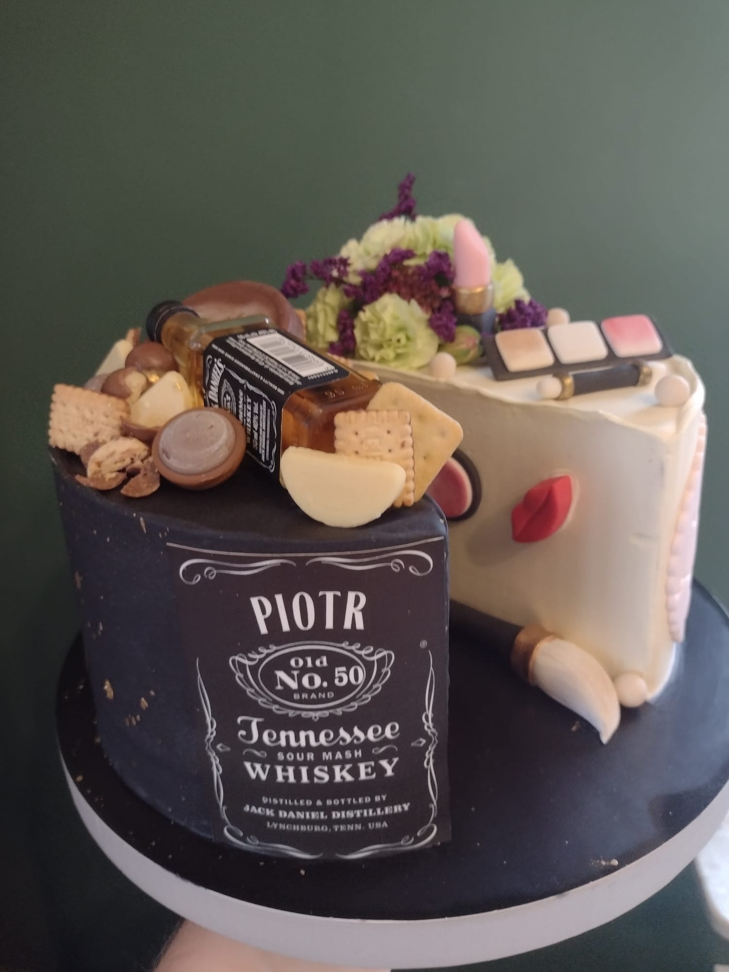 Tort dwuczęściowy: jedna część imituje butelkę whisky Jack Daniel's z napisem 'Piotr Old No. 50', druga część zdobiona motywami makijażu, kwiatami i jadalną miniaturą butelki.