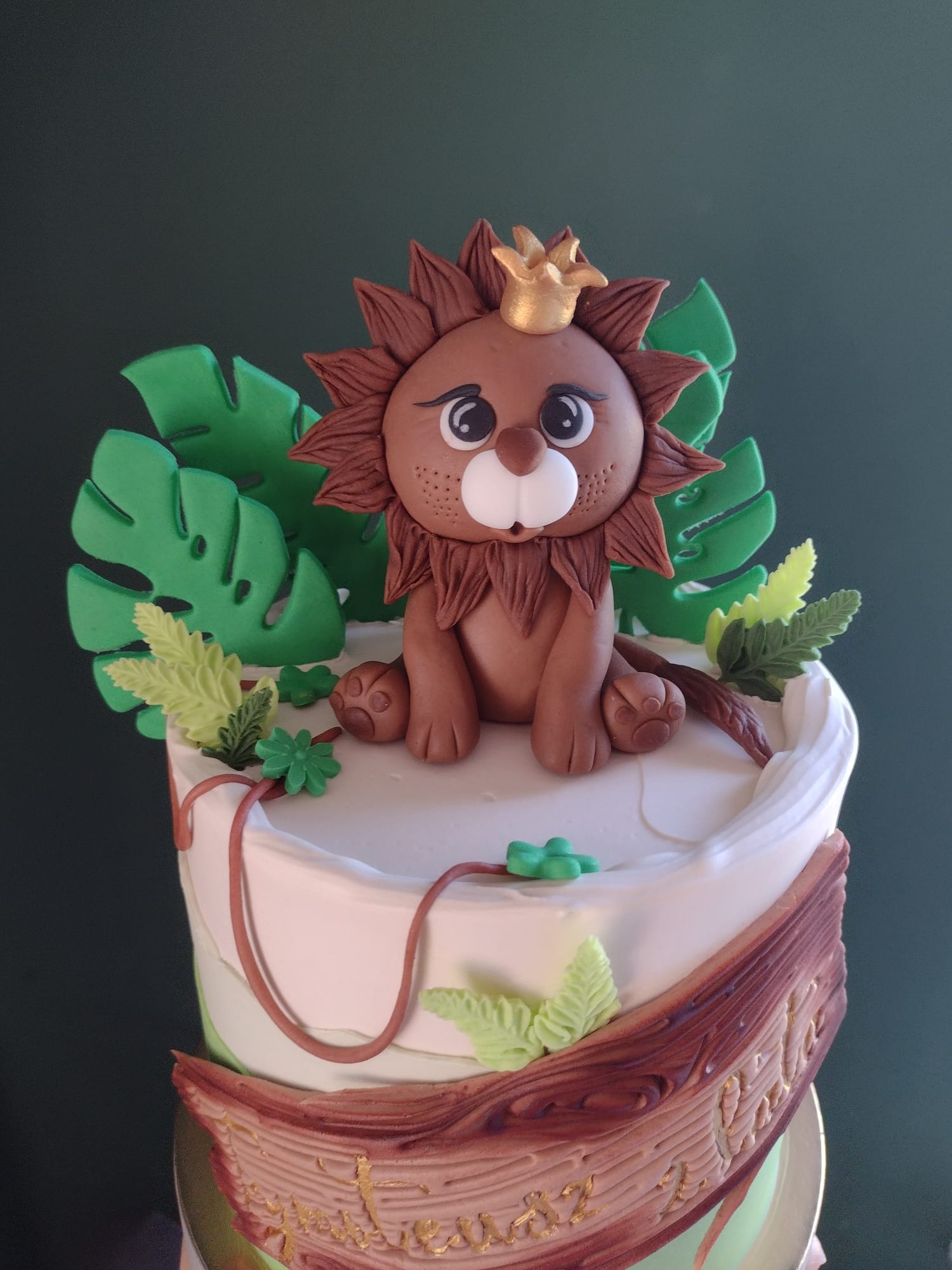 Tort zdobiony figurką lwa w koronie i liśćmi monstery z masy cukrowej, imitujący leśną scenerię.