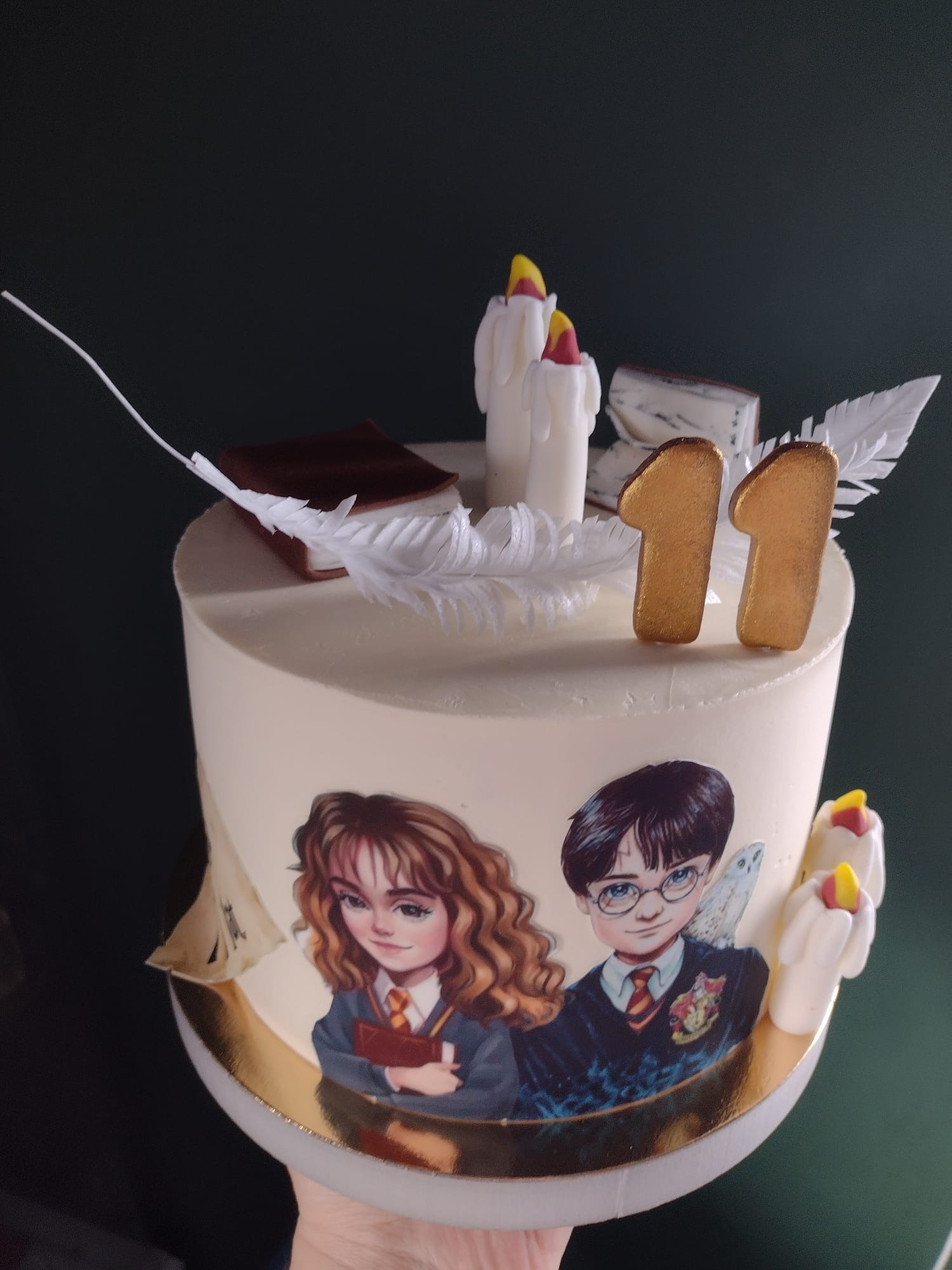 Tort urodzinowy z motywem Harry'ego Pottera, zdobiony figurkami świeczek, piór i liczbą 11, na ciemnym tle.