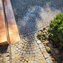 Profesjonalne usługi myjką ciśnieniową - Fragment kostki brukowej, część mokra po czyszczeniu, część sucha, widoczne schody z terakoty i zieleń. Kontrast czystości i zabrudzeń.