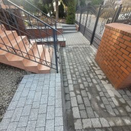 Profesjonalne usługi myjką ciśnieniową - Częściowo umyta kostka brukowa na podjeździe, kontrastująca z brudną powierzchnią. Schody z terakoty i metalowa balustrada. Widoczne ogrodzenie i zieleń w tle.