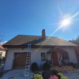 Profesjonalne usługi myjką ciśnieniową - Dom jednorodzinny z brązowym dachem i kominem, drabina oparta o elewację, błękitne niebo i silne słońce. Widok z dołu.