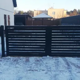 Nowoczesna brama wjazdowa przesuwna z poziomych profili w kolorze antracytowym, widoczna z zewnątrz posesji, na podjeździe pokrytym śniegiem.