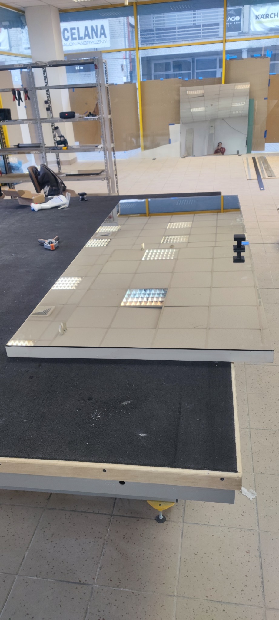 Szkło na stole warsztatowym z przyssawkami, widoczne narzędzia i odblaski sufitu.