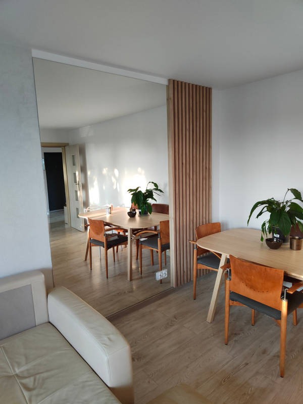 Nowoczesne wnętrze z dużym lustrem w salonie, oddzielającym przestrzeń jadalną z drewnianą ścianką działową z pionowych listew.