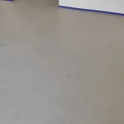 Jasnoszara, gładka posadzka z widocznymi smugami i zabezpieczeniem taśmą malarską przy ścianach.