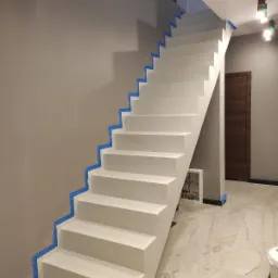 Białe schody z taśmą malarską zabezpieczającą ściany i podłogę, widoczna instalacja w szafce pod schodami i marmurowa podłoga.