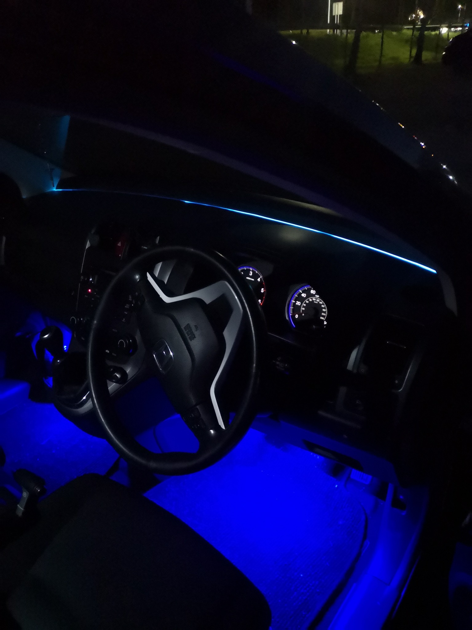 Wnętrze samochodu Honda z podświetleniem LED w kolorze niebieskim na desce rozdzielczej i pod nogami, widoczne zegary i kierownica.