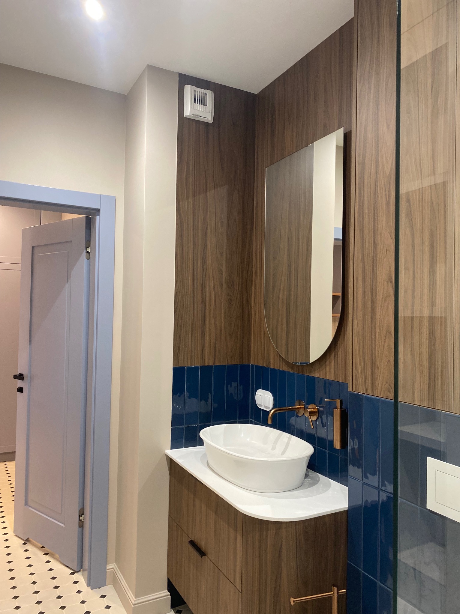 Elegancka łazienka po remoncie: biała umywalka nablatowa, armatura w kolorze różowego złota i ściany wyłożone granatowymi, błyszczącymi płytkami.