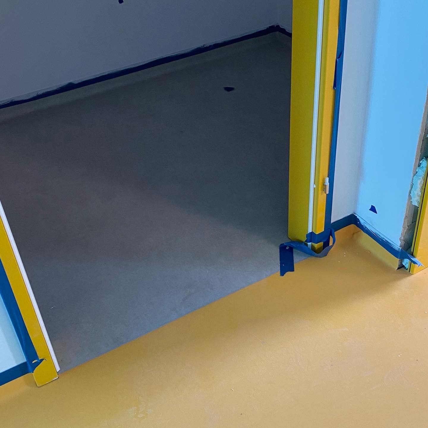 Przygotowane do malowania podłoże z żółtą podłogą i niebieską taśmą malarską zabezpieczającą ściany i futryny.