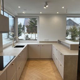 B.art Pracownia Stolarska Bartłomiej Kijowski - Jasna kuchnia z drewnianą podłogą w jodełkę, złote detale armatury i uchwytów, duże okna z widokiem na zimowy krajobraz. Minimalistyczny design.