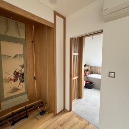 B.art Pracownia Stolarska Bartłomiej Kijowski - Nowoczesne wnętrze z drewnianą zabudową w stylu japońskim: przesuwne drzwi, dekoracyjna wnęka z katanami i obrazem, widok na łazienkę. Jasne kolory, minimalistyczny design.