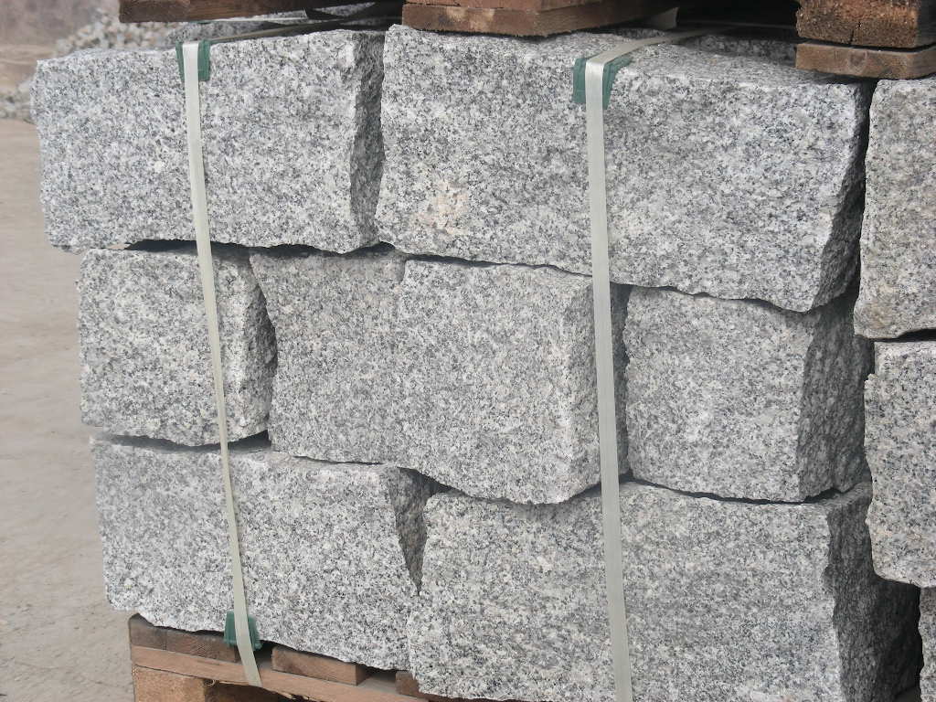 Szare, granitowe sześciany ułożone w stos na palecie, spięte plastikową taśmą, gotowe do transportu.