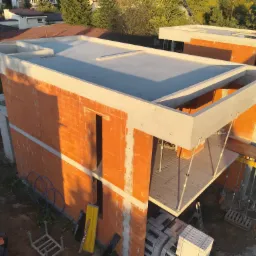 Budowa domu w stanie surowym otwartym z pomarańczowych bloczków, widoczne zbrojenia i szalunki. Ujęcie z góry w słoneczny dzień.